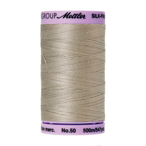 Mettler 50 Weight Silk Finish Cotton Thread 547 yards Drizzle, a spool of beige silk finish cotton thread with purple top and bottom labels.