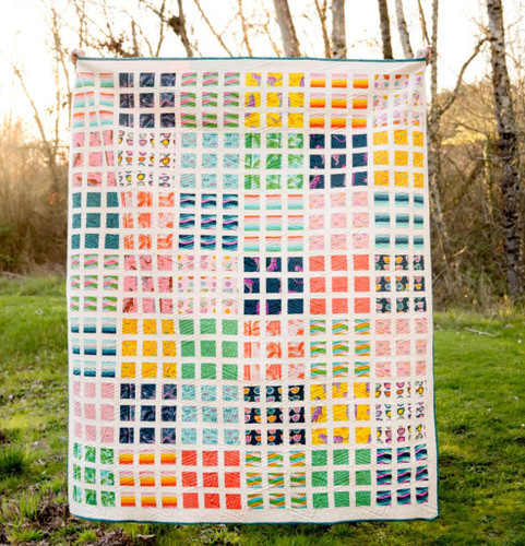 The April Quilt by Kitchen Table Quilts Moda Fabrics Ruby Star Society Poolside Too, colorful quilt displayed outdoors with trees in the background.