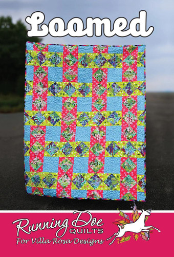 Villa Rosa Designs Loomed Pattern quilt with colorful floral and geometric designs, vibrant pink, green, blue, and yellow colors, displayed outdoors.