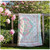 Wilmington Prints Peony Blossoms Queen Sized Quilt Kit, quilt with pink, white, and pastel floral patterns hanging on a wooden fence outdoors with blooming peonies and lush green trees in the background.