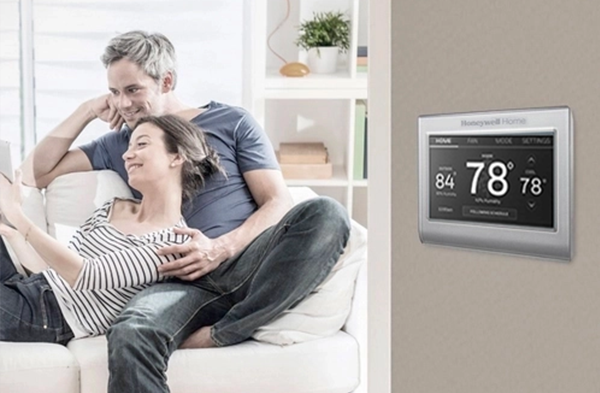 couple on couch with honeywell thermostat on wall