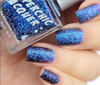 In The Twinkling Of An Eye Nail Polish, close-up of glittery blue nail polish on fingernails with the bottle of the nail polish shown in the background.