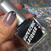 Empowered Thermal Nail Polish, close-up of a hand holding a black nail polish bottle with the Marvel The Adventures In Beauty label and a thumb with a cured nail painted in a gradient mauve to gray nail polish, holographic background.