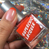 Amused Thermal Nail Polish, a close-up of a person's fingernail with a gradient orange to pink nail color, and a bottle of Superchic Lacquer thermal nail polish held in hand against a colorful, shiny background.