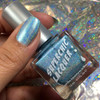 Outbreak Sky Blue Nail Polish, holographic sky blue nail polish in a clear bottle with a silver cap showing holographic reflection in the background.
