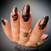 Black Widow Nail Polish - Black Platinum Magnetic + Red Aurora Chrome, close-up of manicured nails with a glossy, holographic finish featuring dark metallic tones and shimmering red highlights.