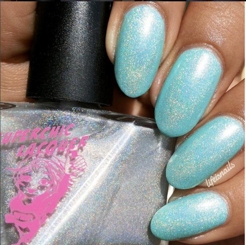 Pleasant Surprise Nail Polish, light blue holographic glitter nail polish applied on fingernails with a black cap bottle visible in the background.