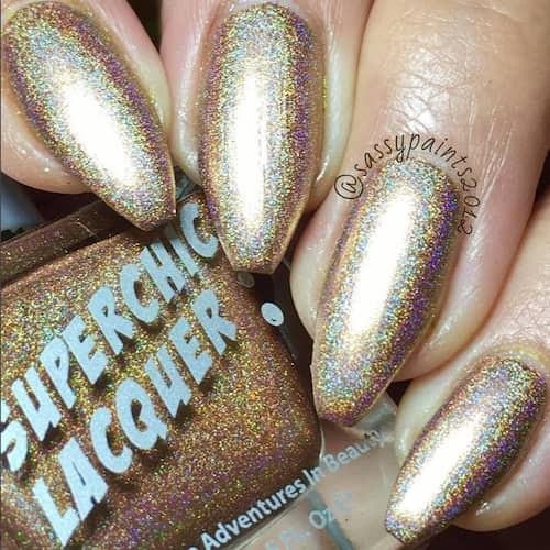 Dart Thru The Heart Nail Polish, close-up of nails painted with holographic gold and purple glitter nail polish.