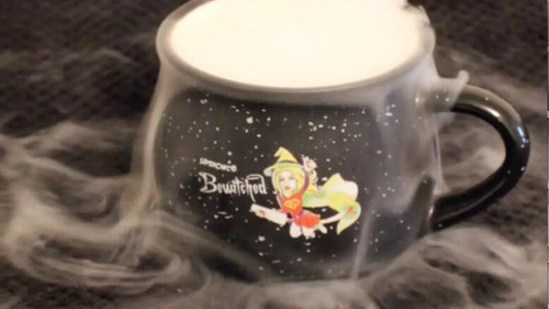 SuperChic® Bewitched Mug - Cauldron Inspired Coffee Mug - 12 Oz, black ceramic mug featuring a whimsical witch flying on a broomstick with the Bewitched logo, surrounded by a foggy, smoky effect.