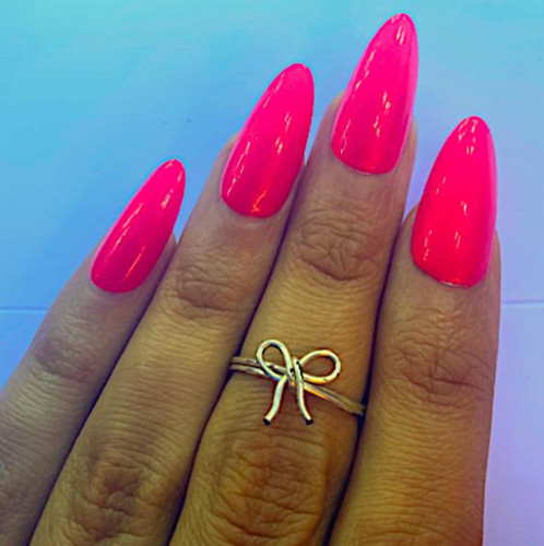 Cherry Bomb Neon Shimmer Nail Polish, vibrant pink neon nails with shimmer finish on a hand with a delicate bow ring.