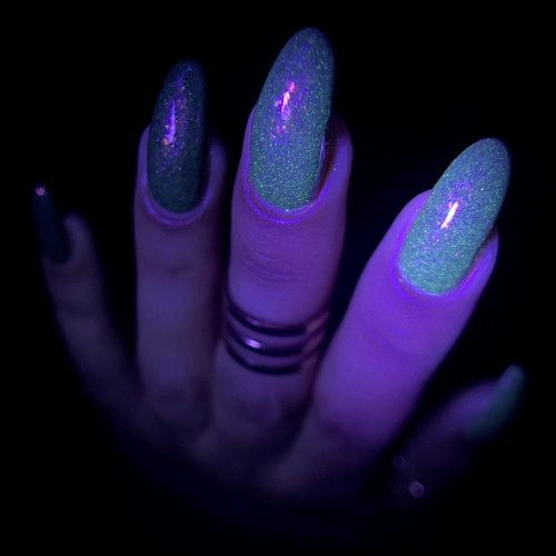 Pumpkin Patch Near Me Halloween Nail Polish, nails glowing under UV light showing vibrant green and blue glittery design.