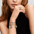 Modelo luciendo el Charm Medallón Búho de Pandora en aleación con chapado en oro junto a otras joyas en mano y pulsera - 764805C01