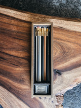 A 12-piece pencil set in an aged pine box with a black cork interior, featuring Matte, 602, Natural, and Pearl pencils, alongside a Grey Two-Step Long Point Sharpener. A 12-piece pencil set in an aged pine box with a black cork interior, featuring Matte, 602, Natural, and Pearl pencils, alongside a Grey Two-Step Long Point Sharpener.