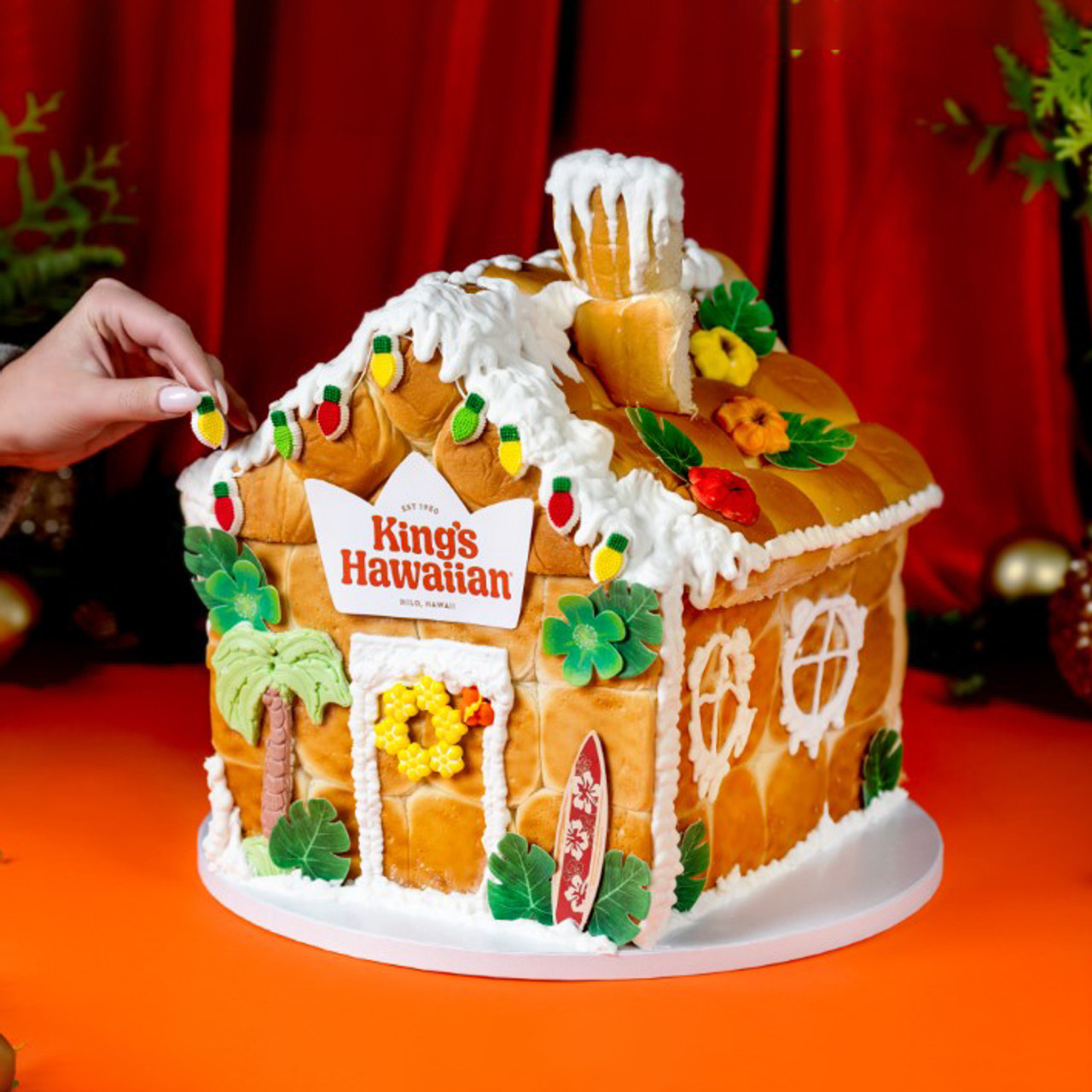 Someone placing the last piece of candy on King's Hawaiian Roll Gingerbread House