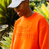Lifestyle image of King's Hawaiian orange crewneck with embossed logo on the chest, front Lifestyle image of King's Hawaiian orange crewneck with embossed logo on the chest, front