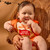 Smiling baby in the King's Hawaiian Original Hawaiian Sweet Rolls baby costume, designed to look like the sweet rolls package, being held in front of a bat garland.