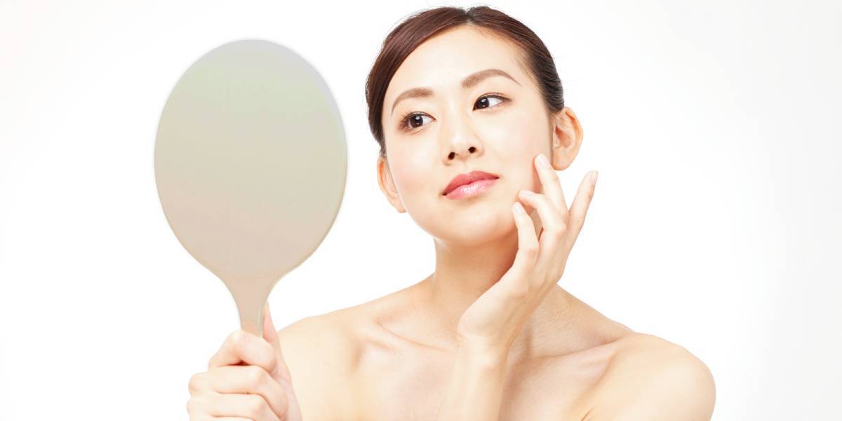 Japanese woman examining her skin with a hand mirror as part of a natural skincare routine