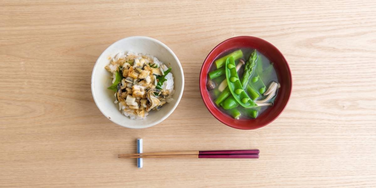 Traditional Japanese ichiju-issai meal with rice topped with seaweed, miso soup in a wooden bowl, and chopsticks on a wooden table