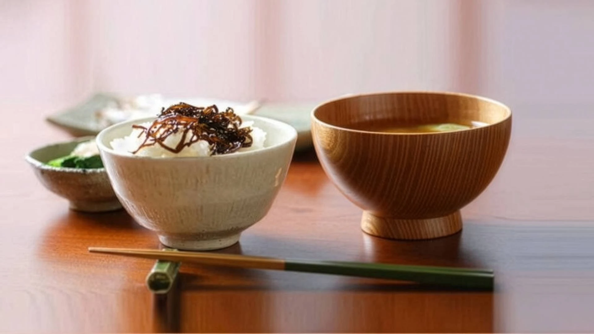 traditional-japanese-one-soup-one-dish-ichiju-issai-meal Traditional Japanese ichiju-issai meal with rice topped with seaweed, miso soup in a wooden bowl, and chopsticks on a wooden table