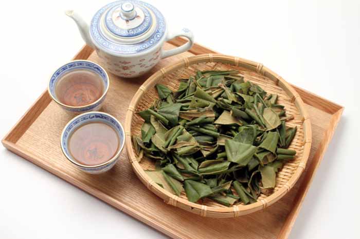 Dried loquat leaves in a basket and cups of tea on a wood tray