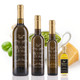 Four Mount Dora Olive Oil Company bottles in descending size stand in a row: a large 750 mL, a 375 mL, a 200 mL, and a small 60 mL sampler with a black label and visible golden-green oil. A bowl of green pesto, basil leaves, and a wedge of Parmigiano sit behind them on a white background.