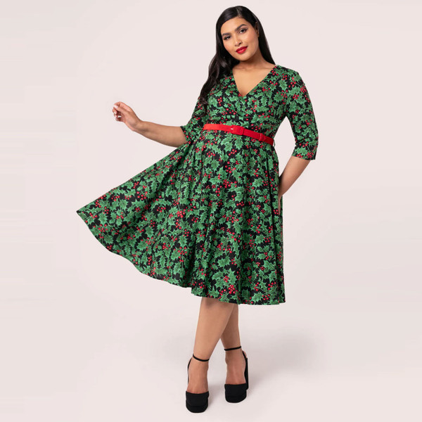 Woman wears Hell Bunny Nicole Christmas Holly Print 50s Doll Dress in Black and Green with flared skirt