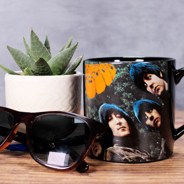 The Beatles Rubber Soul Mug Boxed Mug in Black next to pot plant and sunglasses.