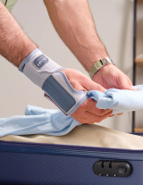 Wrist brace worn while packing luggage, demonstrating stability and protection during travel tasks.