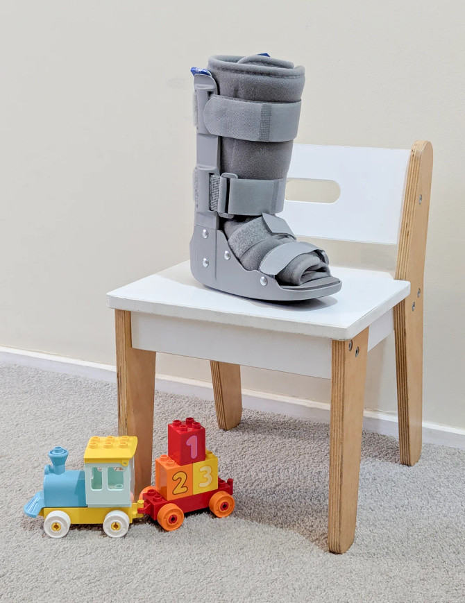 Paediatric walker boot placed on chair with toys, illustrating child-friendly recovery support in a home environment.