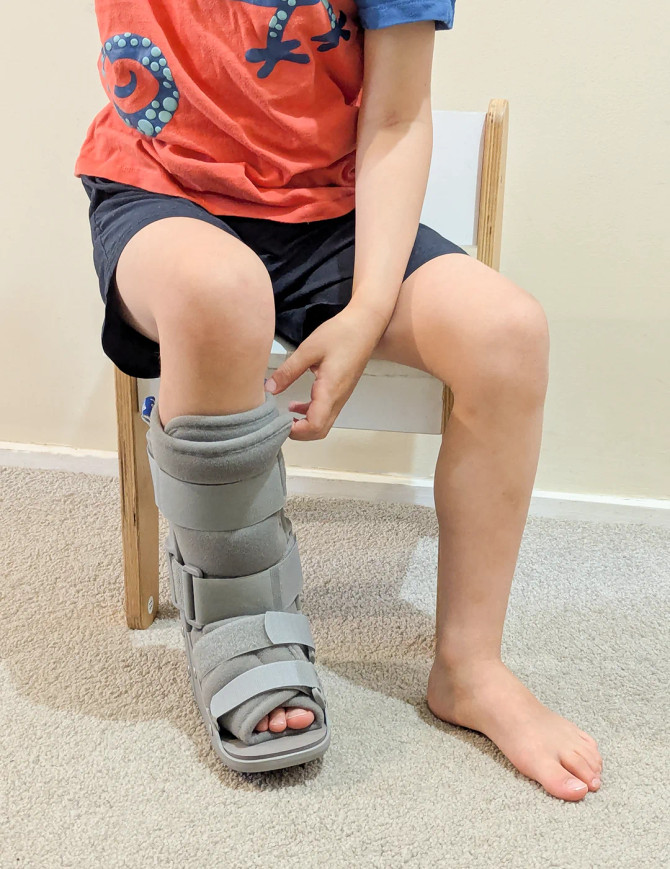 Child seated wearing paediatric walker boot, showing stability and protection for everyday movement.