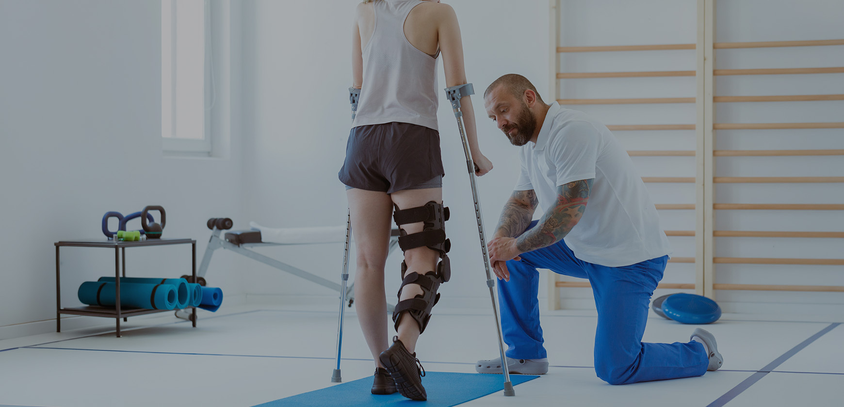 Physiotherapist assisting a patient walking with crutches while wearing a knee rehabilitation brace during physiotherapy treatment.