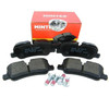Mintex Rear Brake Pads for Discovery 4 3.0 TDV6, close-up of the brake pad with black backing plate and metal clip, with red Mintex packaging in the background.