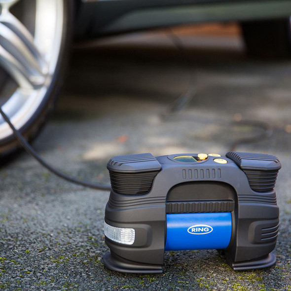 Ring Automotive Ring 12V Rapid Digital Tyre Inflator Compressor RAC830, portable electric tyre inflator on outdoor asphalt ground near car wheel.