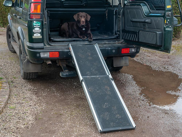 Britpart Dog Ramp Telescopic Lightweight Non Slip for 4x4's Vans Cars, a black folding ramp with aluminum sides extended from the back of a green vehicle, with a black dog lying on the ramp.