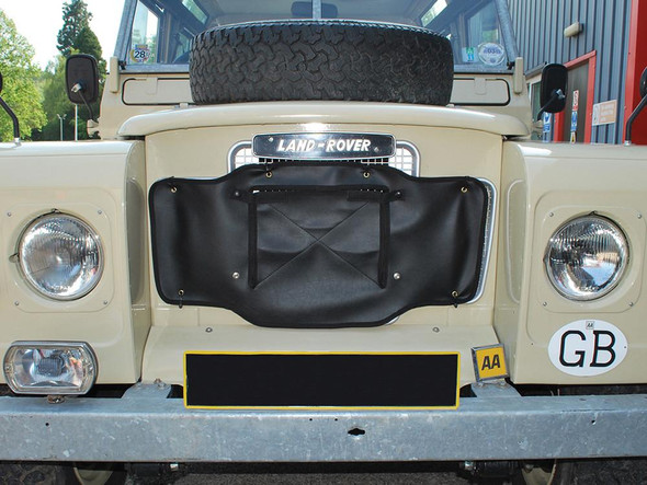 Britpart Black Radiator Muff for Series 2A Late Models and Series 3, front view of a Land Rover vehicle showing the radiator cover attachment on the grille with a spare tire on top.