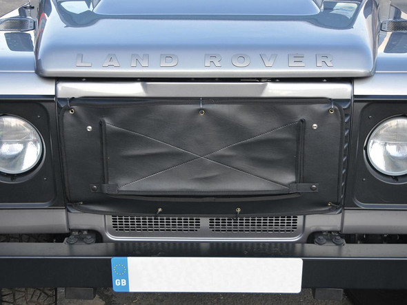 Britpart Radiator Muff Black for Defender (1986-2016), black radiator cover/muff installed on front of Land Rover Defender vehicle.