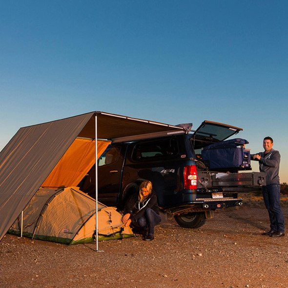 ARB 4X4 Accessories Expedition Awning Front Wind Break 2.5m ARB, outdoor camping setup with vehicle and tents at sunset, showcasing the awning installed on a vehicle with wind break for camping comfort.