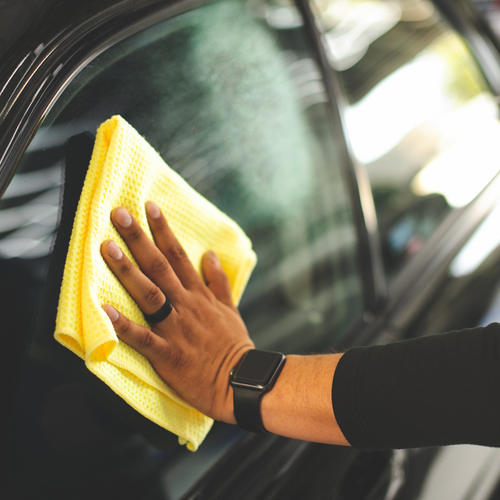 Cleaning black car window using yellow waffle weave microfiber towel for crystal-clear glass