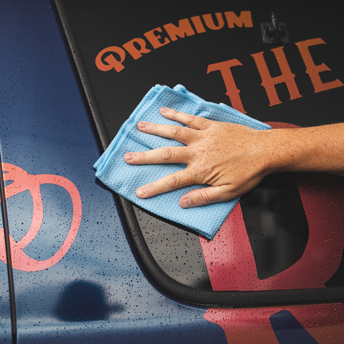 Cleaning car window with light blue waffle weave microfiber towel near graphic vinyl deca