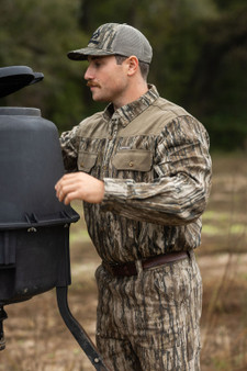 Men's Milk River Button Down Camo Shirt in Realtree Legacy shown in use outdoors, highlighting the relaxed fit and dual chest pockets.