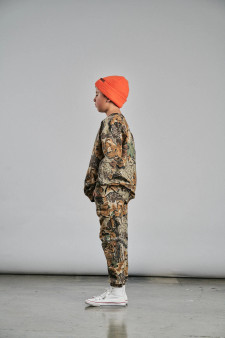 Child wearing Realtree Advantage Classic camo sweatpants with matching sweatshirt and bright orange beanie, shown in side view against a neutral background.