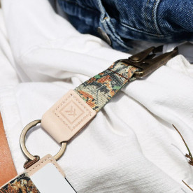 A camouflage-patterned fabric lanyard with beige leather accents, featuring an embossed “K” logo, a metal clasp, and a round metal key ring.