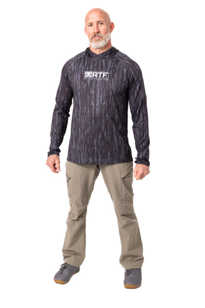 A man is shown wearing the Realtree Fishing Men's Hooded Black Shirt in a full-body front view, highlighting the shirt’s black Original camo pattern and front RTF logo.
