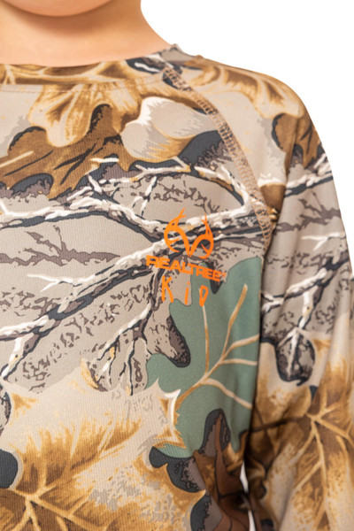 Close-up of the chest area on the kid’s Realtree Advantage Classic long-sleeve shirt showing the orange Realtree Kid logo printed over the camo pattern.