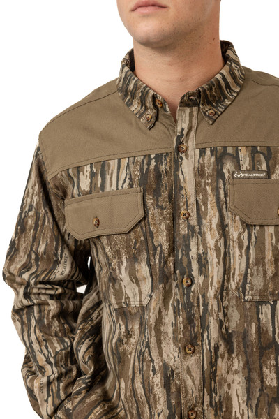 Men's Milk River Button Down Camo Shirt in Realtree Legacy shown from an angled front view, emphasizing collar construction and pocket layout.