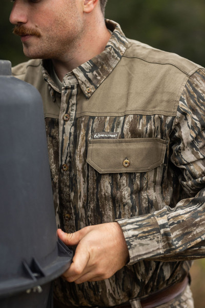 Close-up of the Men's Milk River Button Down Camo Shirt showing the reinforced solid yoke, button-flap chest pocket, and Realtree logo.
