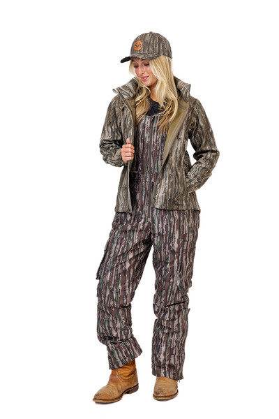 Full-body view of a woman wearing the Realtree Legacy camo hunting jacket layered over matching hunting bibs, showing overall outfit fit.