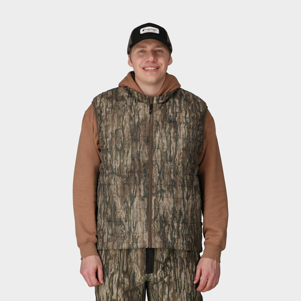 Model wearing Realtree Legacy camo PrimaLoft vest layered over brown hoodie, front view.