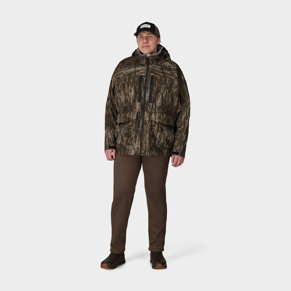Man wearing Frogg Toggs Oxbow jacket in Realtree Legacy camo, front view with hood up and zippered pockets visible.