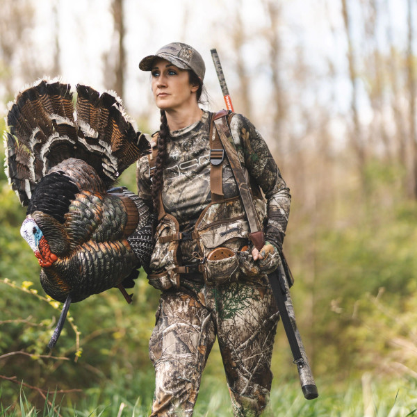 Hunter wearing DSG Outerwear turkey vest in Realtree EDGE camo carrying a harvested turkey in the field.